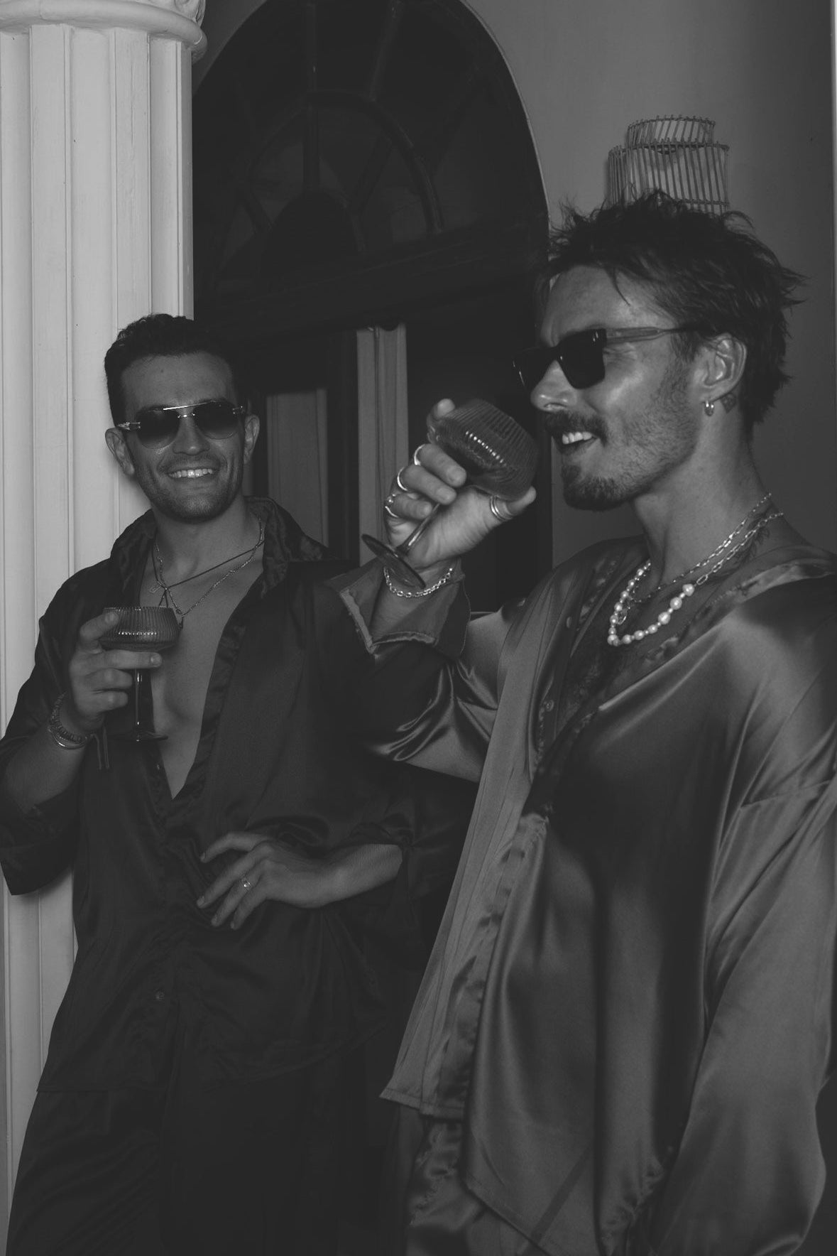 Two men in silk-inspired black outfits by Armè, toasting in a luxury night setting – ESSENZA VOL.1 campaign